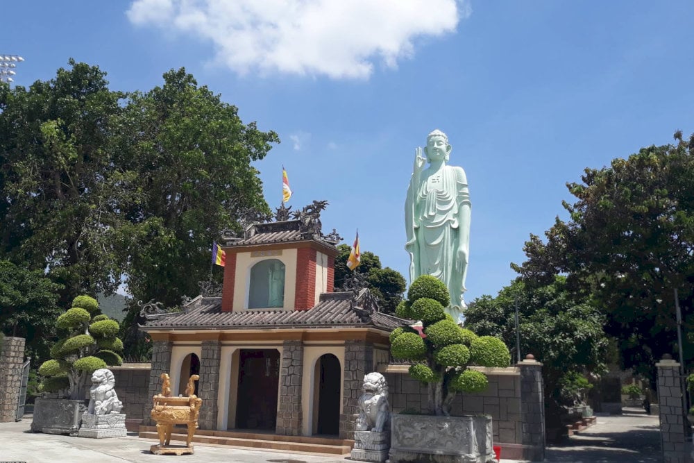 The Tam Quan gate is built of sturdy green stone, behind it is the statue of Amitabha Buddha